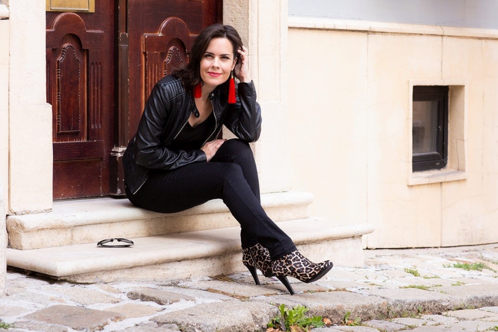 Alexandra Vrábelová sitting on stone steps in a stylish black outfit with a leather jacket and leopard-print heels, smiling confidently outdoors. Source: Alexandra Vrábelová