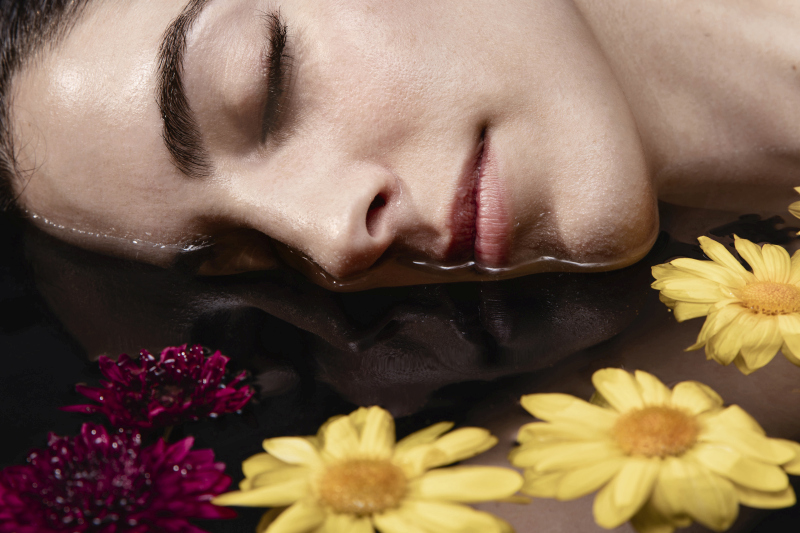 Close-up of a woman’s face resting in water surrounded by colorful flowers, symbolizing natural beauty rituals and spa-inspired skincare; Source: https://www.freepik.com/free-photo/close-up-beautiful-young-woman-relaxing_7291342.htm