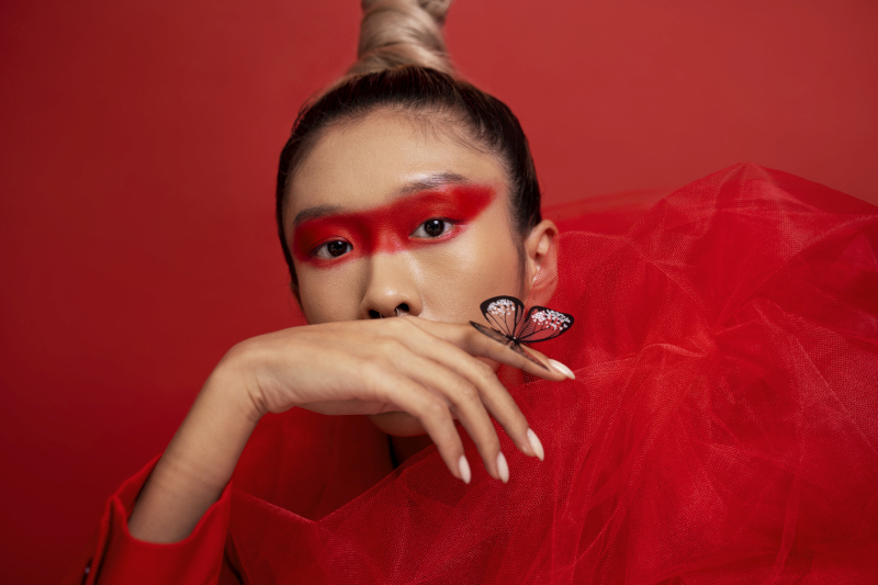 Portrait of a woman with bold red eye makeup and long manicured nails, inspired by traditional beauty aesthetics and beauty rituals around the world.; Source: https://www.freepik.com/free-photo/surrealist-portrait-fashionable-woman_21541565.htm