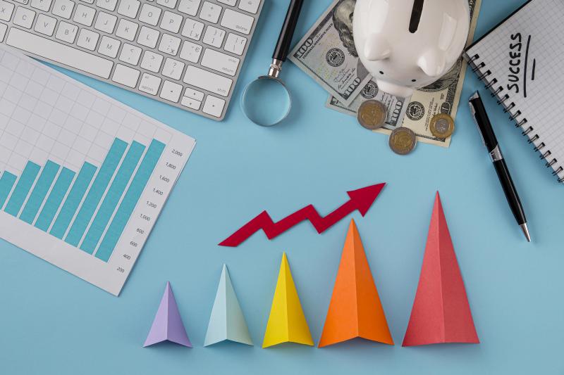 Flat lay of business desk with financial charts, piggy bank, coins, and a rising arrow above colorful paper bars, symbolizing pricing strategy, profit growth, and business planning. Source: https://www.freepik.com/free-photo/top-view-business-items-with-growth-chart-colored-cones_11383283.htm