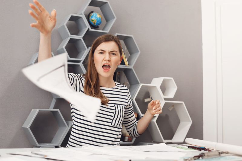 Frustrated woman throwing papers in the air at her desk, expressing overwhelm and rejection of unimportant tasks; Source: https://www.freepik.com/free-photo/close-up-portrait-young-unhappy-good-looking-female-freelance-engineer-throwing-work-papers-away-with-angry-unsatisfied-expression-after-customer-declined-all-work_8357731.htm