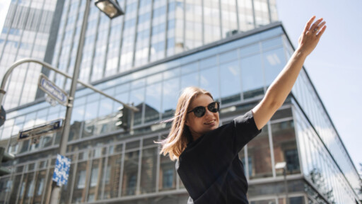 Young woman in sunglasses raising her arm confidently in a modern city, symbolizing independence and financial freedom. Source: https://www.freepik.com/free-photo/image-beauty-woman-sunglasses-smiling-camera_28000459.htm