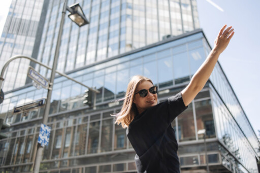 Young woman in sunglasses raising her arm confidently in a modern city, symbolizing independence and financial freedom. Source: https://www.freepik.com/free-photo/image-beauty-woman-sunglasses-smiling-camera_28000459.htm