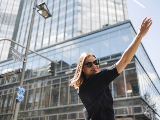Young woman in sunglasses raising her arm confidently in a modern city, symbolizing independence and financial freedom. Source: https://www.freepik.com/free-photo/image-beauty-woman-sunglasses-smiling-camera_28000459.htm