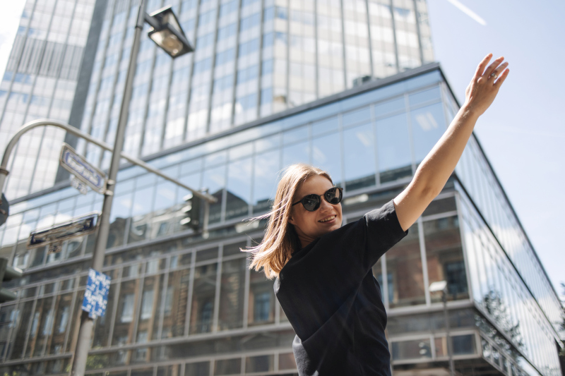 Young woman in sunglasses raising her arm confidently in a modern city, symbolizing independence and financial freedom. Source: https://www.freepik.com/free-photo/image-beauty-woman-sunglasses-smiling-camera_28000459.htm