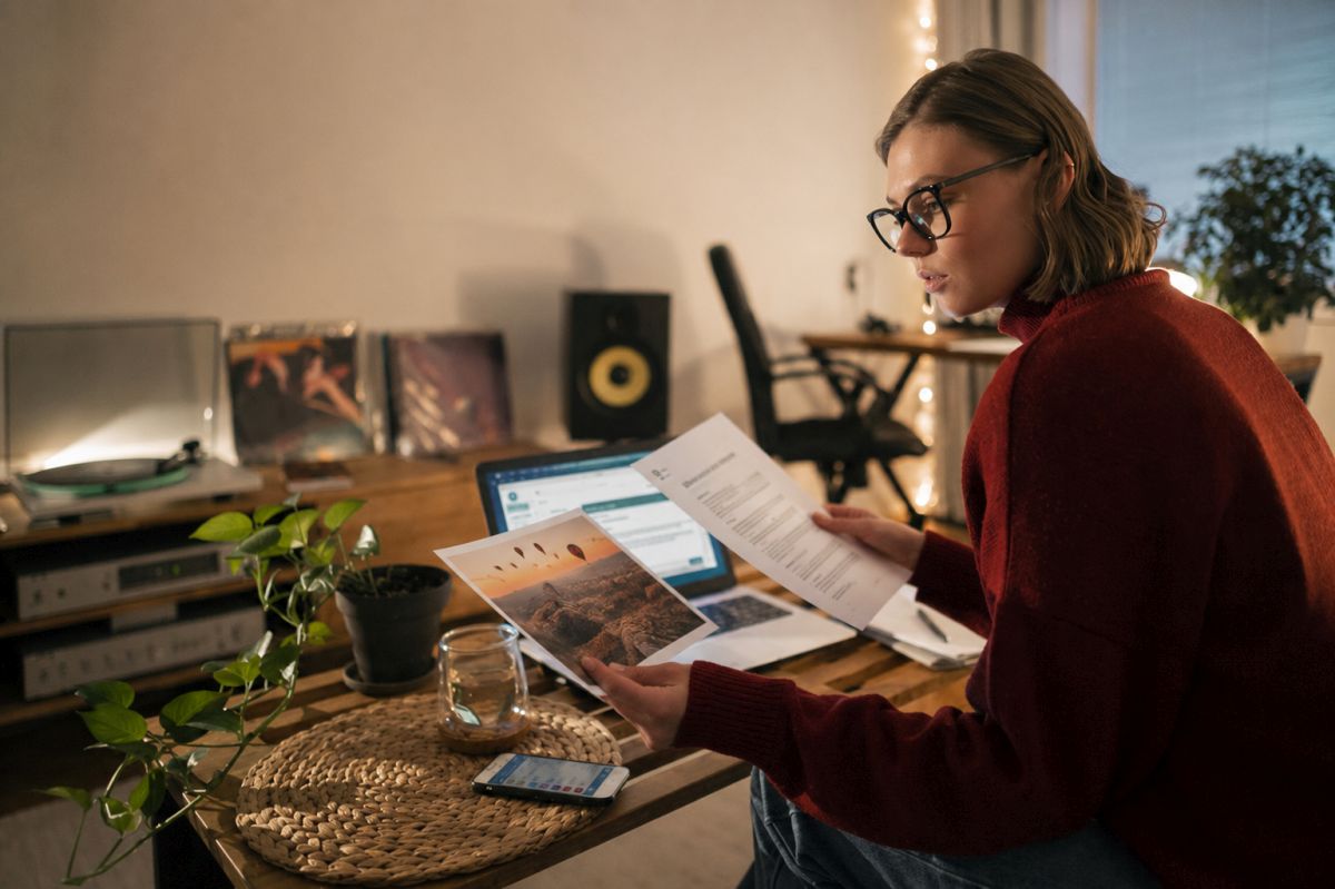 Woman reviewing a document and photograph while working from a cozy home office. Source: https://www.magnific.com/free-photo/person-working-late-night-from-home_36294703.htm Image edited with AI