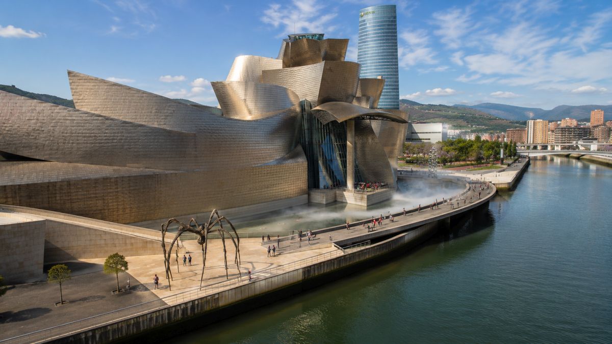 The Guggenheim Museum Bilbao in Spain, featuring its iconic titanium-clad curves beside the Nervión River, with visitors exploring the waterfront promenade. Image created with AI
