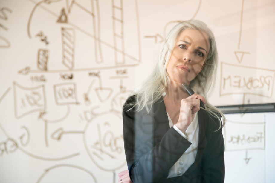 Businesswoman thinking in front of a glass board covered with diagrams while developing a strategic plan; Source: https://www.magnific.com/free-photo/attractive-businesswoman-looking-statistic-data-thinking-confident-experienced-thoughtful-female-manager-holding-marker-standing-office-room-strategy-business-management-concept_9648864.htm
