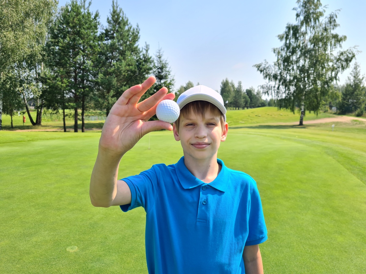 Boy holding up a golf ball while standing on a sunny golf course. Source: https://www.magnific.com/premium-photo/young-boy-holding-golf-ball_225865094.htm