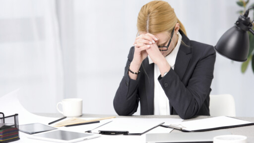 A frustrated businesswoman sitting at her desk with paperwork, a tablet, and a laptop. Source: https://www.magnific.com/free-photo/frustrated-young-businesswoman-workplace-with-paper-digital-tablet-laptop-desk_4048021.htm
