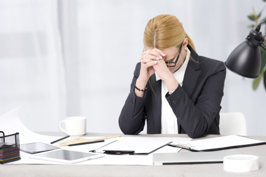 A frustrated businesswoman sitting at her desk with paperwork, a tablet, and a laptop. Source: https://www.magnific.com/free-photo/frustrated-young-businesswoman-workplace-with-paper-digital-tablet-laptop-desk_4048021.htm