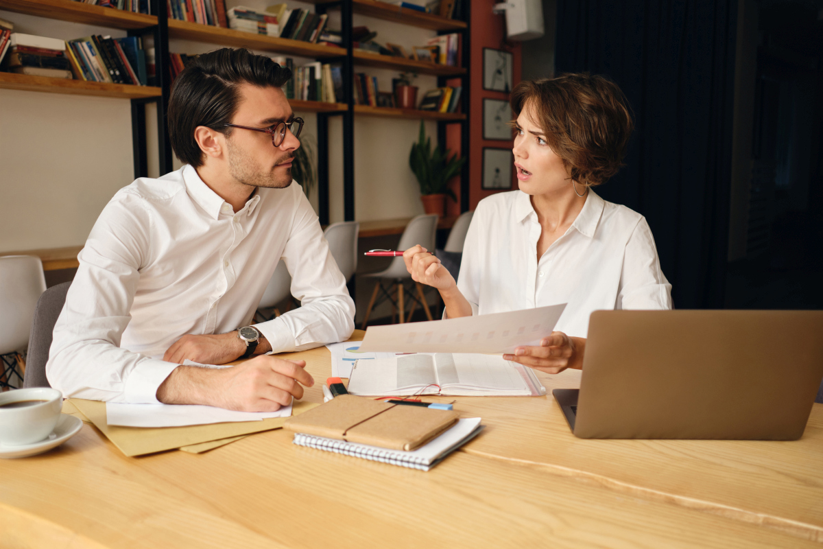 Two business colleagues discussing a project at a table with a laptop, documents, and notebooks. Source: https://www.magnific.com/free-photo/young-business-colleagues-emotionally-discussing-new-project-while-sitting-table-with-laptop-papers-modern-office_25237222.htm