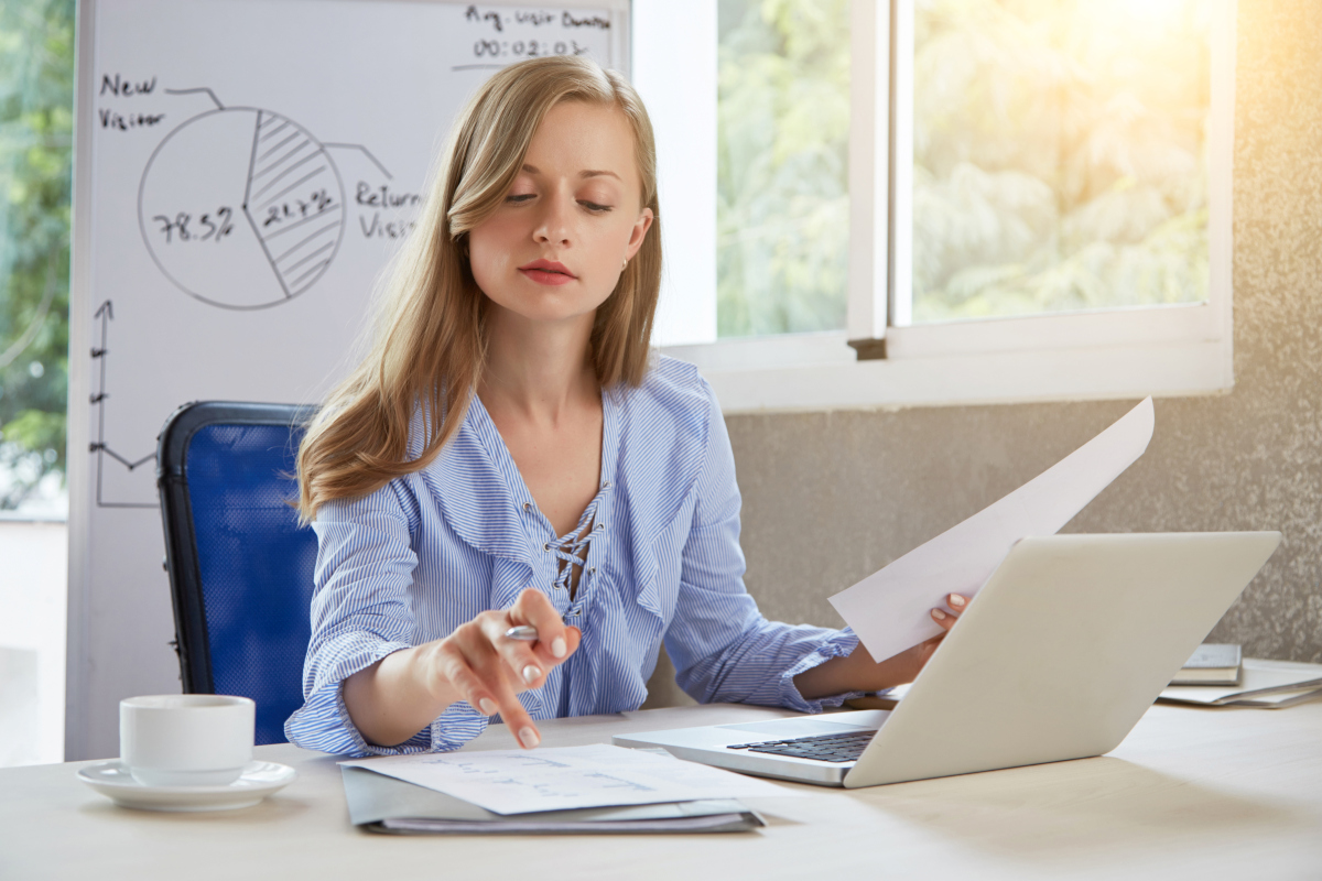 A female entrepreneur reviewing financial documents beside her laptop in a bright office. Source: https://www.magnific.com/free-photo/waist-up-shot-young-blond-businesslady-working-office-desk_6850098.htm