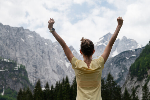 Woman raising her arms in triumph while overlooking a dramatic mountain landscape. Source: https://www.magnific.com/premium-photo/young-woman-standing-beautiful-rocky-mountains-with-her-arms-raised-high_16173706.htm