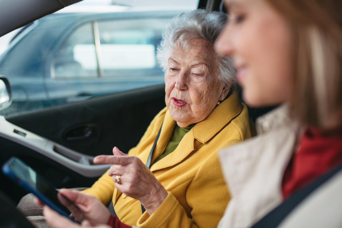 Older woman pointing at a smartphone while sitting in a car with a younger driver. Source: https://www.magnific.com/premium-photo/granddaughter-driving-her-elderly-grandmother-car-taking-her-doctor-shopping-bank-caregiver-driving-elderly-lady-church_371384330.htm