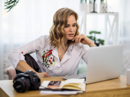 Woman working on a laptop at home with a camera and notebook on her desk, representing a portfolio career with multiple professional roles. Source: https://www.magnific.com/premium-photo/girl-photographer-looks-pictures-laptop-table-with-notepads-phone-camera-room_26710219.htm