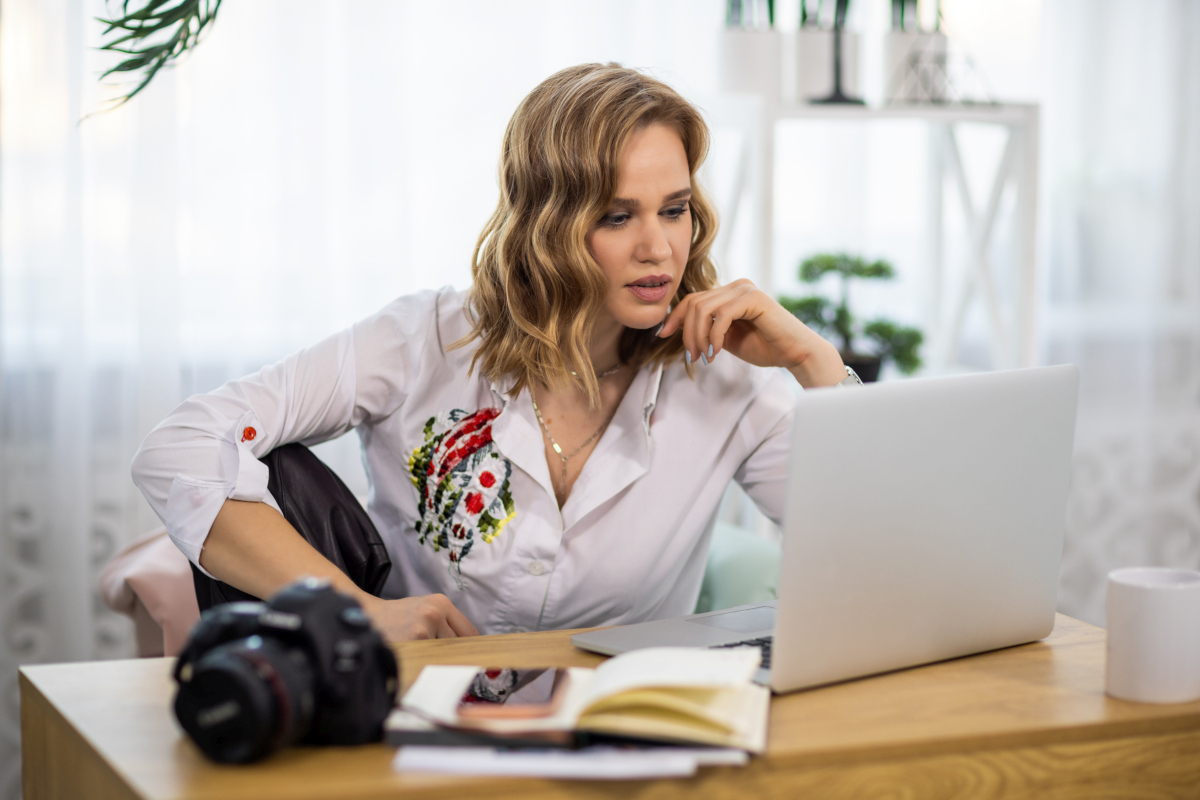 Woman working on a laptop at home with a camera and notebook on her desk, representing a portfolio career with multiple professional roles. Source: https://www.magnific.com/premium-photo/girl-photographer-looks-pictures-laptop-table-with-notepads-phone-camera-room_26710219.htm
