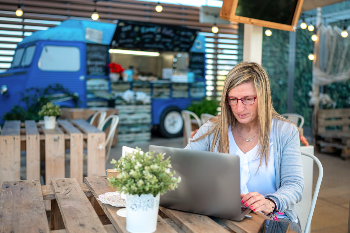 Woman working on a laptop with a food truck in the background, representing a flexible portfolio career. Source: https://www.magnific.com/premium-photo/middle-aged-woman-with-laptop-outdoor-food-stall_22919463.htm 