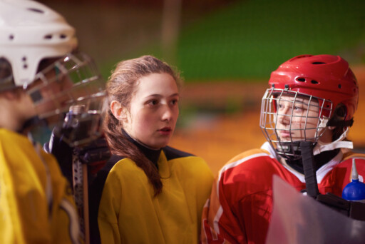 young female hockey players listening to their teammates during a break in the game. Source: https://www.magnific.com/premium-photo/young-teen-girls-ice-hockey-players-team-group-meeting-with-trainer-sport-arena-indoors_36361130.htm